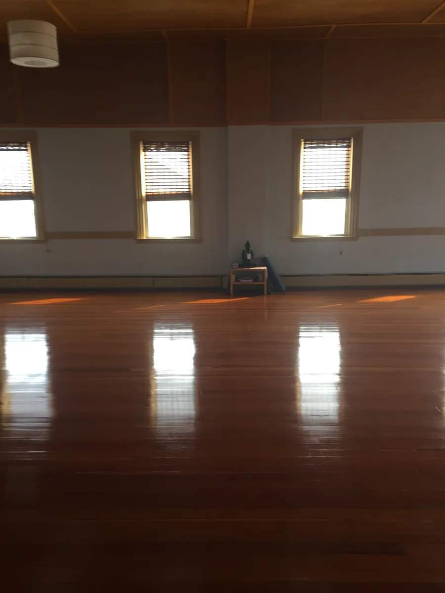 Empty studio with polished wood floors, tall windows and a small Buddha altar against the wall